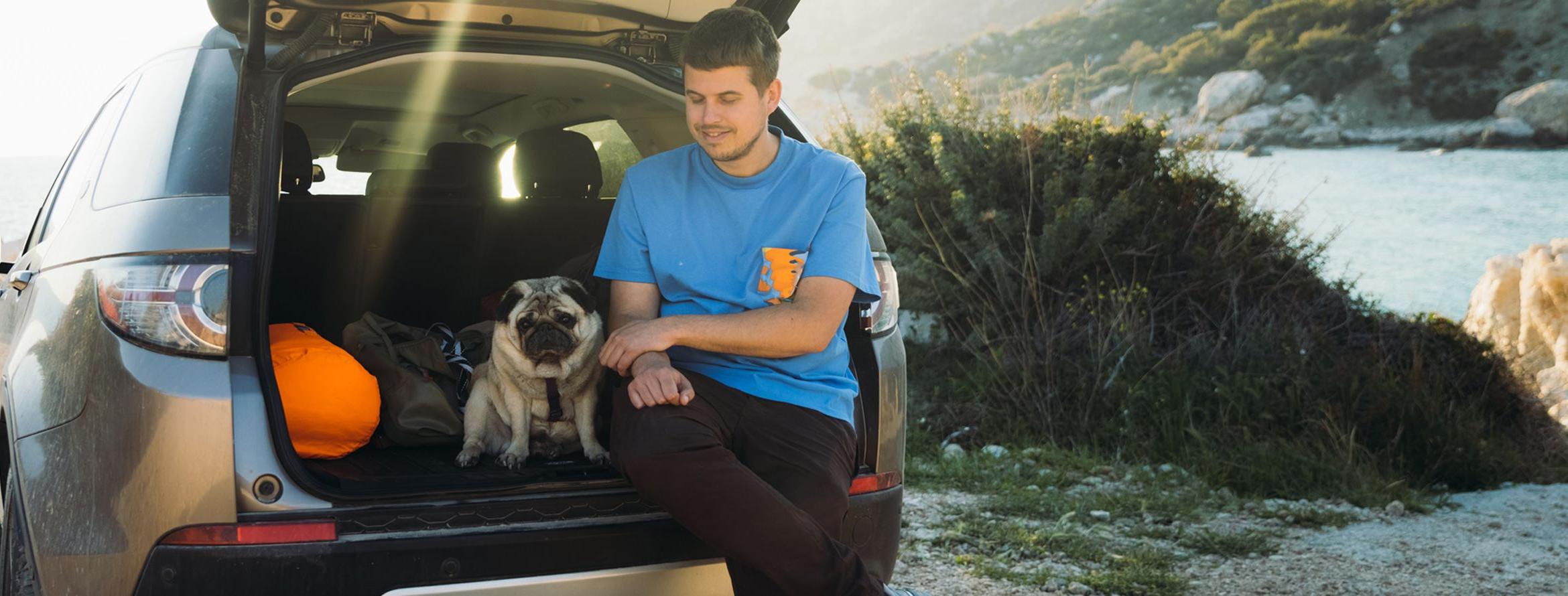 A hiker pets a pug in the back of his new car.