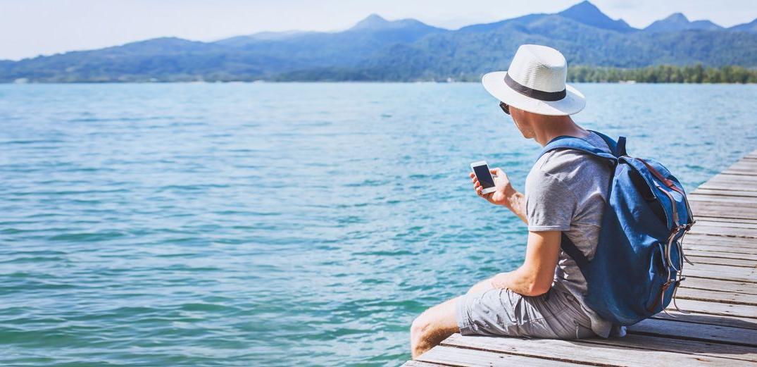 A man checks his Patelco Online account while enjoying a lake view from the edge of a dock.