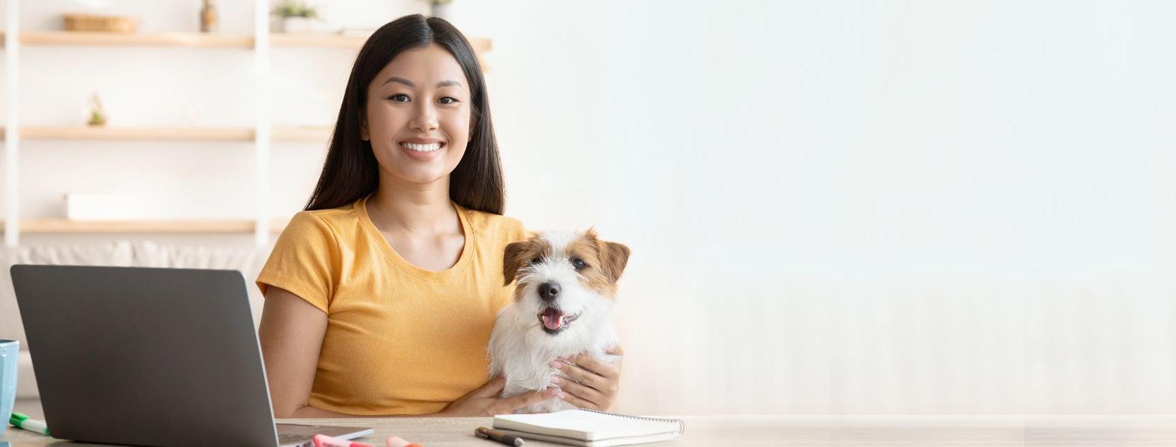 A smiling woman with her dog in her lap signs into Patelco Online from her home laptop.