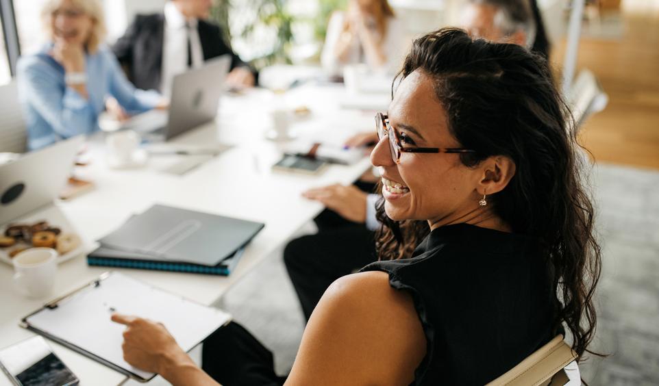 A woman smiles with her coworkers at a conference table.